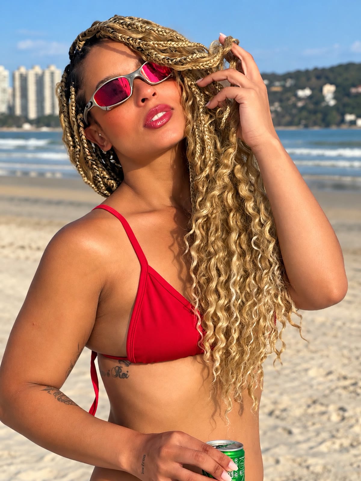 Sarah Fernanda na praia com óculos vermelhos e tranças loiras